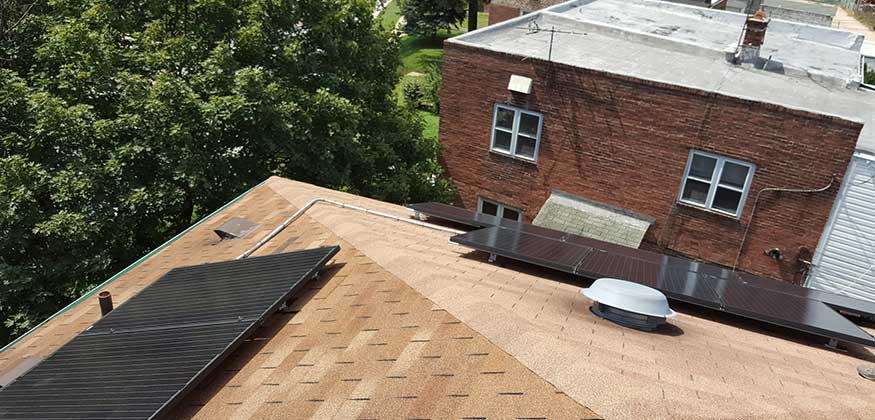 Rooftop solar panels beside a brick building and trees